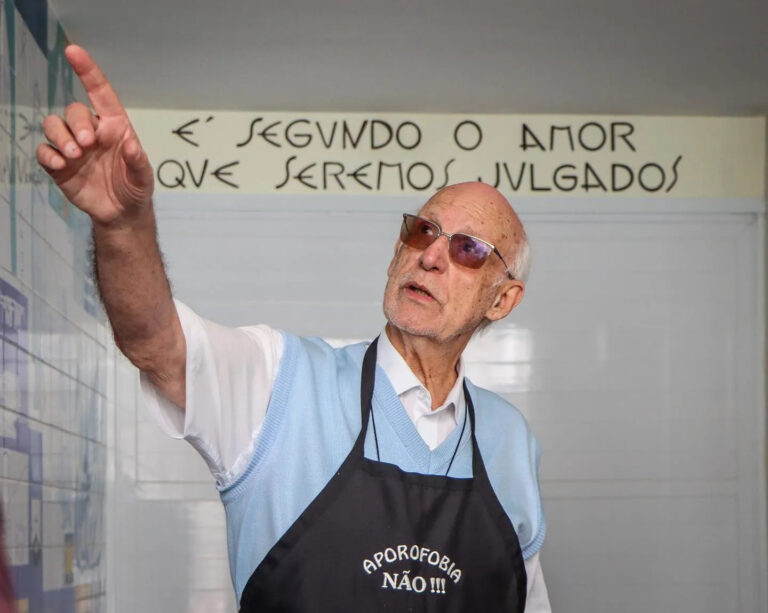 Padre Julio Lancelotti. A mensagem na parede diz: "É SEGUNDO O AMOR QUE SEREMOS JULGADOS". A mensagem no avental é "APOROFOBIA NÃO !!!", um termo que significa aversão ou preconceito contra pessoas pobres. Foto: Divulgação Facebook