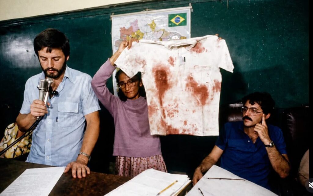 Dona Olinda Tavares, mãe de Padre Josimo, na companhia do Pe. Ricardo Resende e Domingos Furlan na UFRJ, denunciando as mortes no Campo inclusive a morte do filho. Ano de 1986. Foto: Acervo Memorial Padre Josimo